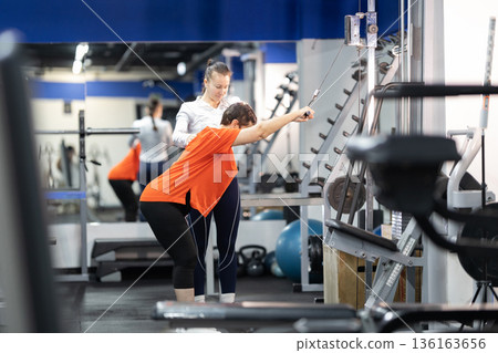 Woman exercising with personal trainer on cable pulldown machine 136163656