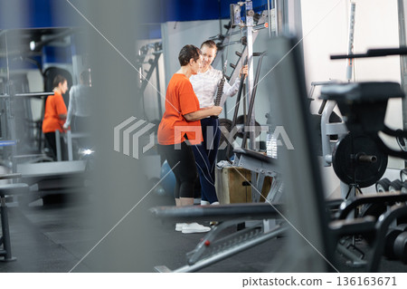 Personal trainer guiding woman exercising on gym machine 136163671