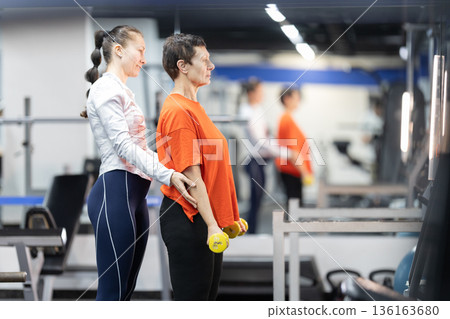 Personal trainer guiding senior woman lifting dumbbells 136163680