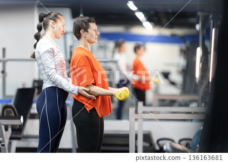Senior woman exercising with personal trainer support 136163681