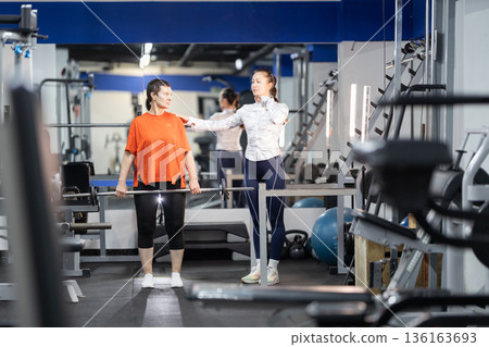 Woman receiving personal trainer guidance for weightlifting workout Woman receiving personal trainer guidance for weightlifting workout 136163693