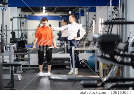 Personal trainer guiding senior woman with barbell training 136163694