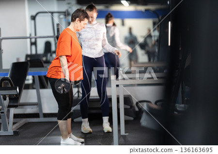 Senior woman training with personal trainer, lifting weights 136163695