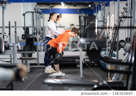 Personal trainer assisting woman with resistance training in gym Personal trainer assisting woman with resistance training in gym 136163697