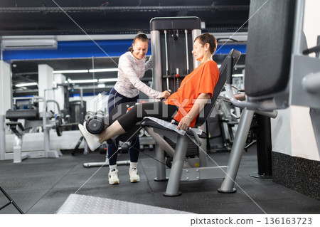 Personal trainer guiding senior woman working out in gym 136163723