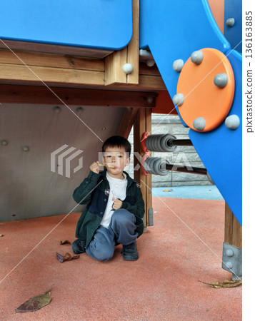 Child Enjoying A Snack Under A Playground Structure In Bright Colors 136163885