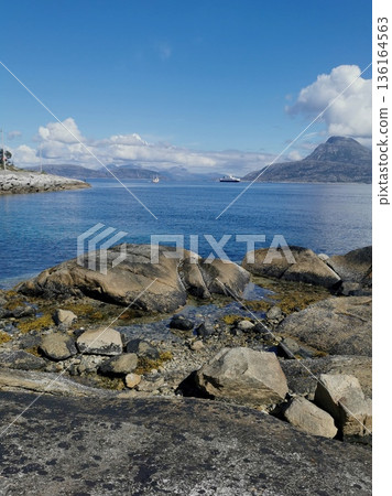 green meadow with houses on a fjord coast and mountains with clouds in the distance, norway 136164563