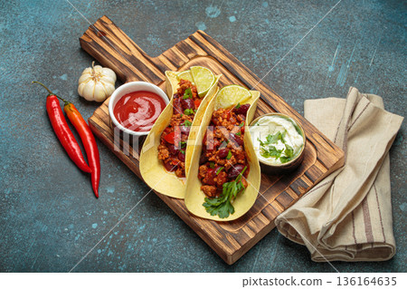 Mexican tacos with chili con carne, red beans, and lime wedges on wooden board top view 136164635