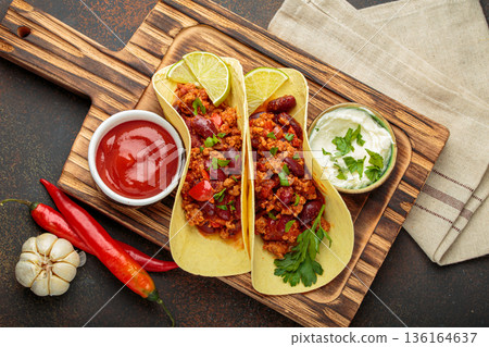 Mexican chili con carne tacos with lime, ketchup, sour cream and fresh herbs on wooden board top view Mexican chili con carne tacos with lime, ketchup, sour cream and fresh herbs on wooden board top view 136164637