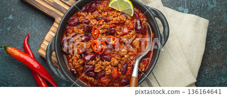 Mexican dish Chili con carne with lime, garlic and chili pepper on dark background top view Mexican dish Chili con carne with lime, garlic and chili pepper on dark background top view 136164641