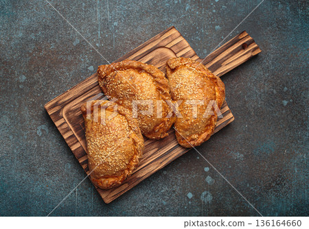 Delicious baked empanadas with sesame seeds served on wooden board with sauces, traditional Spanish savoury pastry 136164660