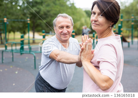 elderly man and woman do gymnastics on an outdoor sports ground elderly man and woman do gymnastics on an outdoor sports ground 136165018
