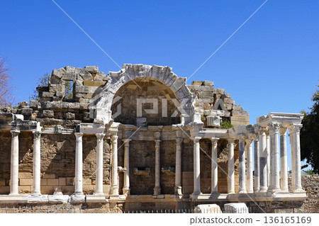 Ancient Ruins of a Stunning Historical Structure Showcasing Arched Architecture and Classical Columns Against a Clear Blue Sky Ancient Ruins of a Stunning Historical Structure Showcasing Arched Architecture and Classical Columns Against a Clear Blue Sky 136165169