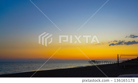 A Serene Evening at the Beach: Captivating Colors of Sunset Reflecting on the Calm Ocean with a Pier in the Distance 136165178