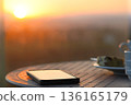 Serene Evening Scene: A Smartphone, Delicious Treat, and Sunset Reflection on a Table with Relaxing Ambiance 136165179