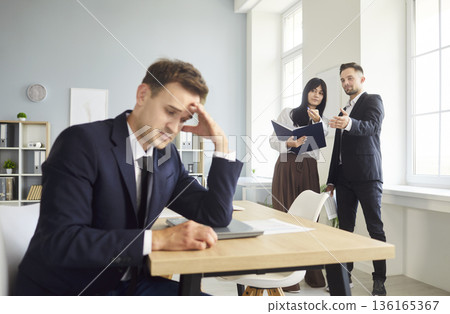 Upset employee at desk while colleagues spread gossips, office conflict 136165367