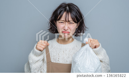 一名女子拿著垃圾袋，看到裡面的垃圾散發著難聞的氣味，沉甸甸的，不禁皺了皺眉頭。 136165822