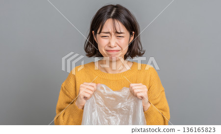 一位婦女抱著垃圾袋，神情痛苦，眼眶含淚。 136165823