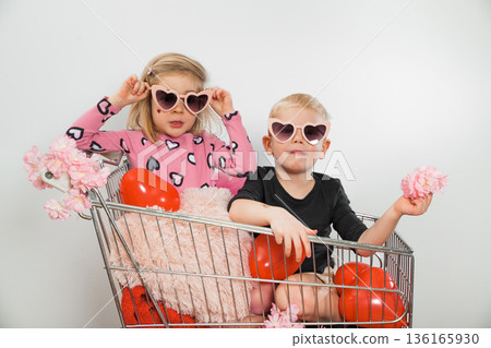 Kids enjoy shopping cart fun with heart sunglasses and balloons in a studio 136165930