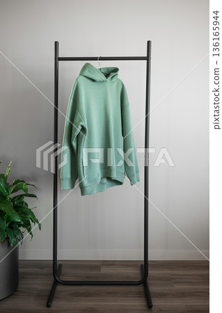 Hooded sweatshirt hanging on a black rack beside a green plant in a modern room Hooded sweatshirt hanging on a black rack beside a green plant in a modern room 136165944