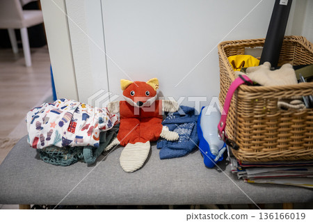 Stuffed animal toy on ironing board with laundry basket, clothes and home cleaning items 136166019