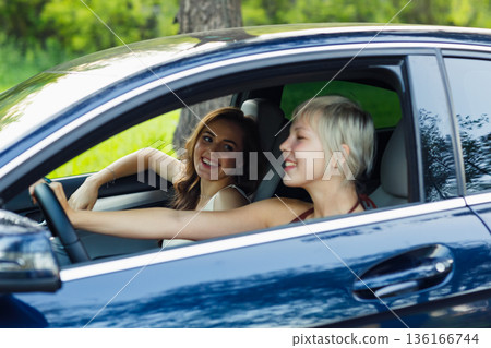 Two woman drivers at car smiling. Cute young happy female driving car vehicle Two woman drivers at car smiling. Cute young happy female driving car vehicle 136166744