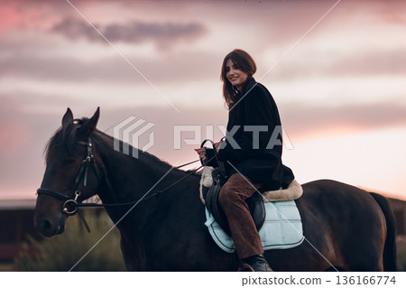 Young woman in black with her horse at sunset outdoors 136166774