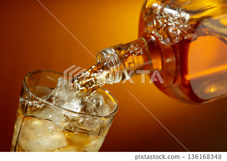 Bottle of whiskey pouring into a glass with ice. 136168348