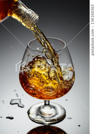 The amber-gold strong alcoholic beverage is poured into a glass. The amber-gold strong alcoholic beverage is poured into a glass. 136168363