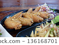 Close up of golden brown crispy fried chicken wings generously topped with fried garlic served on black plate with shredded cabbage and carrot salad side. 136168701