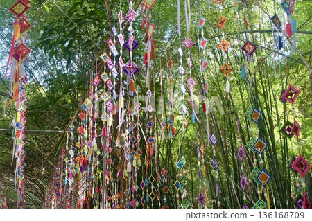 Vibrant handmade silk spiderweb flags, used in a Northeastern Thai Buddhist ritual to capture evil spirits, adorn a lush bamboo grove, symbolizing spiritual protection and rich cultural traditions. Vibrant handmade silk spiderweb flags, used in a Northeastern Thai Buddhist ritual to capture evil spirits, adorn a lush bamboo grove, symbolizing spiritual protection and rich cultural traditions. 136168709