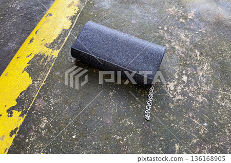 lost black glitter clutch purse with silver chain and rhinestone detail abandoned on a wet concrete ground next to a yellow painted curb 136168905