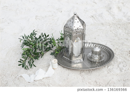 Silver Moroccan Lantern with Candle on Metal Tray, Lentisk Branches and Neutral White Sand Background. Minimal Rustic Still Life, Mediterranean Decor. Ramadan, Eid Mubarak Holiday, Wedding Concept Silver Moroccan Lantern with Candle on Metal Tray, Lentisk Branches and Neutral White Sand Background. Minimal Rustic Still Life, Mediterranean Decor. Ramadan, Eid Mubarak Holiday, Wedding Concept 136169366