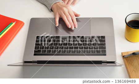 Top view of a female hand on a laptop touchpad at a white desk, close-up. Remote education or work, research, browsing, internet search. Top view of a female hand on a laptop touchpad at a white desk, close-up. Remote education or work, research, browsing, internet search. 136169489