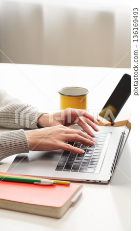 VERTICAL VIDEO: Woman typing on a laptop at a white desk. Remote work, study, and modern productivity. VERTICAL VIDEO: Woman typing on a laptop at a white desk. Remote work, study, and modern productivity. 136169493