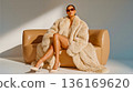 A woman sitting on a couch wearing a fur coat and sunglasses 136169620