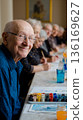 A group of older people sitting at a table with watercolor paints 136169627