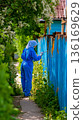 A woman in a blue coverall painting a blue fence 136169629