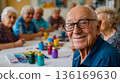 An older man smiling at the camera while sitting at a table with other older people 136169630