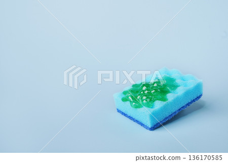 Blue cleaning sponge soaking green dishwashing liquid on blue background Blue cleaning sponge soaking green dishwashing liquid on blue background 136170585