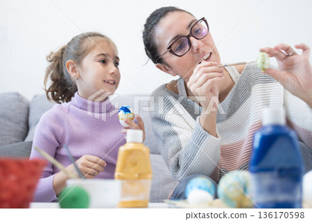 Mother and daughter painting Easter eggs at home. 136170598