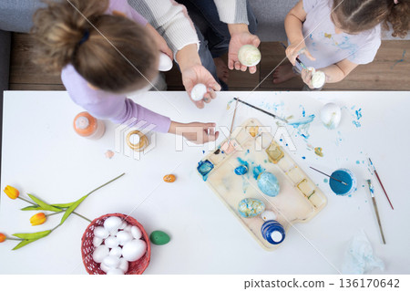 Mother and two daughters painting Easter eggs 136170642