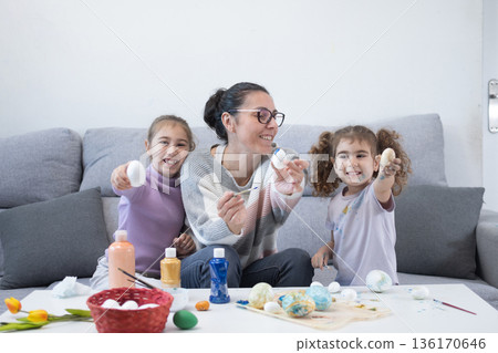 Mother and two daughters painting Easter eggs 136170646