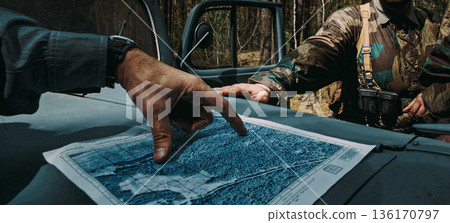 German Army officers looking at a topographic map to plan a route. Hands pointing at a location on paper placed on a car hood. Historical reconstruction of the Wehrmacht operations. 136170797