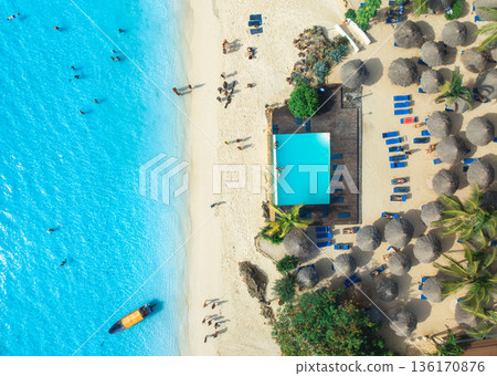 Aerial view of pool, sandy beach, palms, umbrellas, boat, ocean Aerial view of pool, sandy beach, palms, umbrellas, boat, ocean 136170876