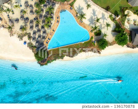 Aerial view of pool, sandy beach, umbrellas, boat, blue sea 136170878