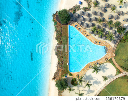 Aerial view of pool, sandy beach, umbrellas, boat, blue sea Aerial view of pool, sandy beach, umbrellas, boat, blue sea 136170879