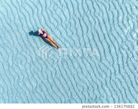 Aerial view of woman in bikini and white hat lying in blue sea 136170882