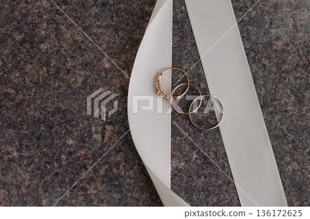 Wedding rings on white ribbon on dark stone surface Wedding rings on white ribbon on dark stone surface 136172625