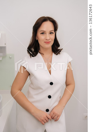 Portrait of skilled female cosmetologist smiling looking at camera, wearing uniform and conveying professionalism, expertise and caring patient-focused aesthetic medicine service in beauty clinic. Portrait of skilled female cosmetologist smiling looking at camera, wearing uniform and conveying professionalism, expertise and caring patient-focused aesthetic medicine service in beauty clinic. 136172643